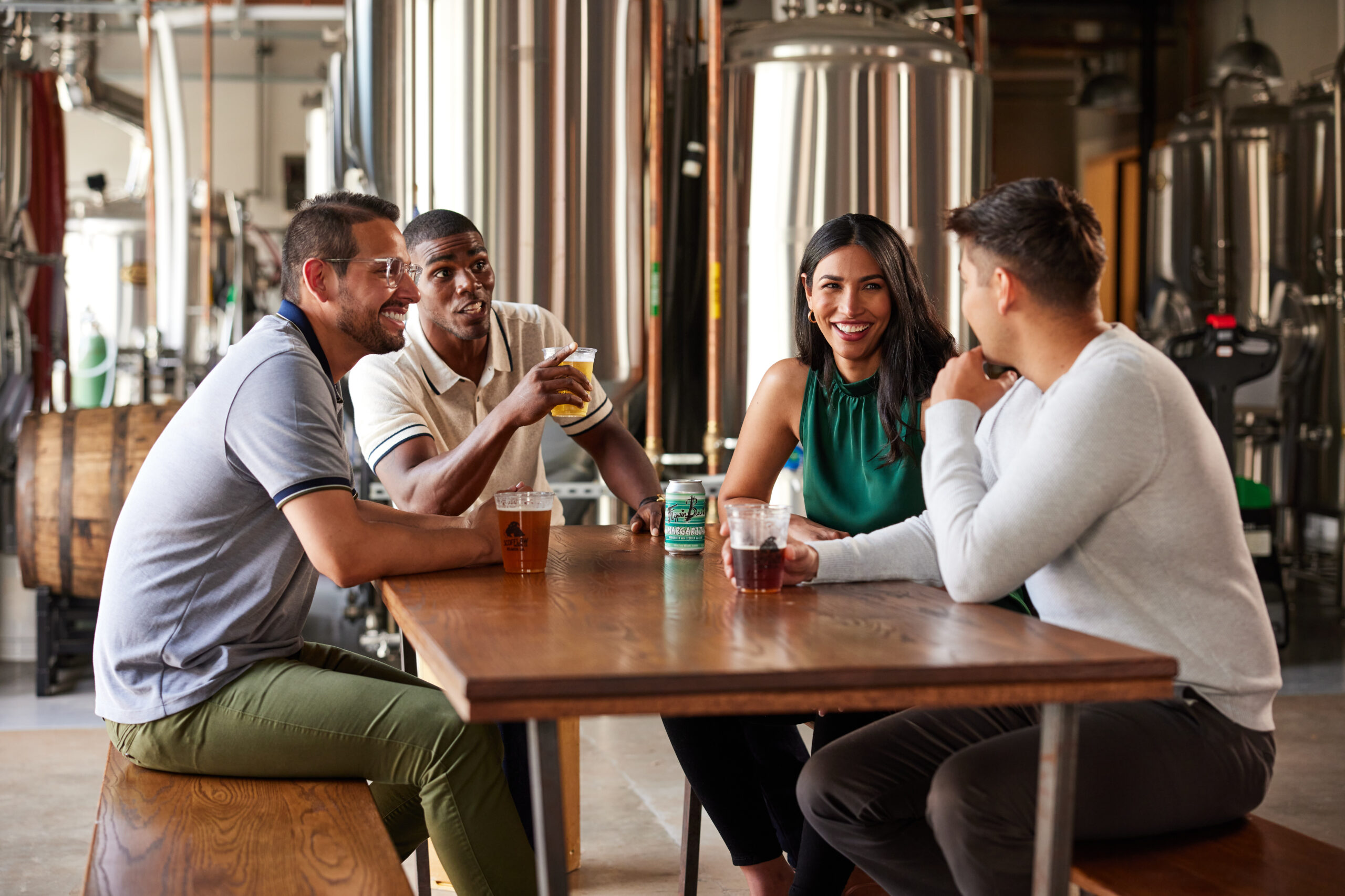 Group of three men and one woman sitting at a table inside a brewery