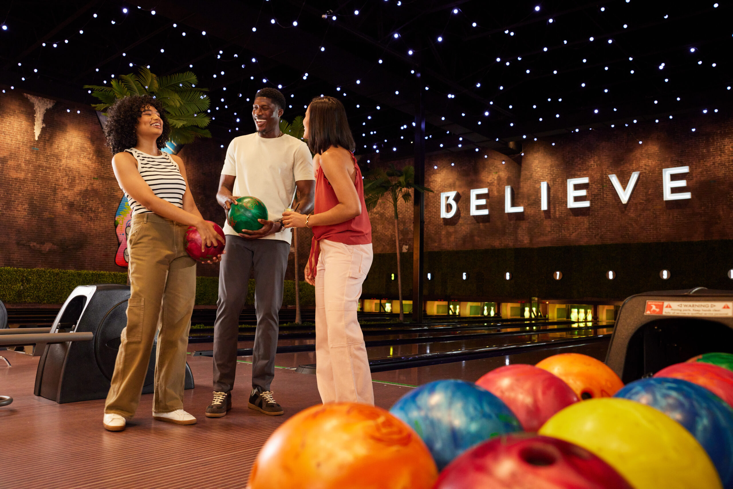 Group of two women and one man holding bowling balls in a bowling alley